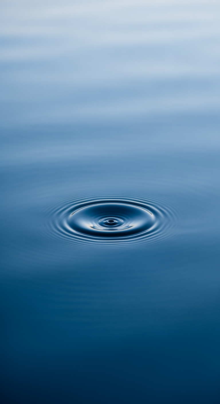 A close-up view of a calm water surface with a single, gentle ripple expanding from the center, indicating a small disturbance.